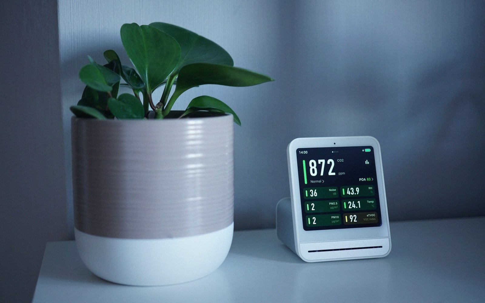 Air quality monitor displaying CO2, humidity and VOC readings beside a potted plant