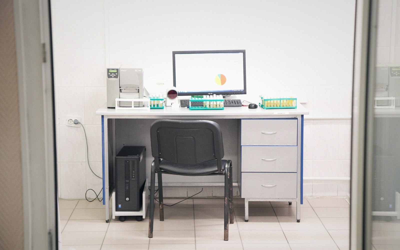 Empty lab desk with computer monitor, test tube racks and a black office chair