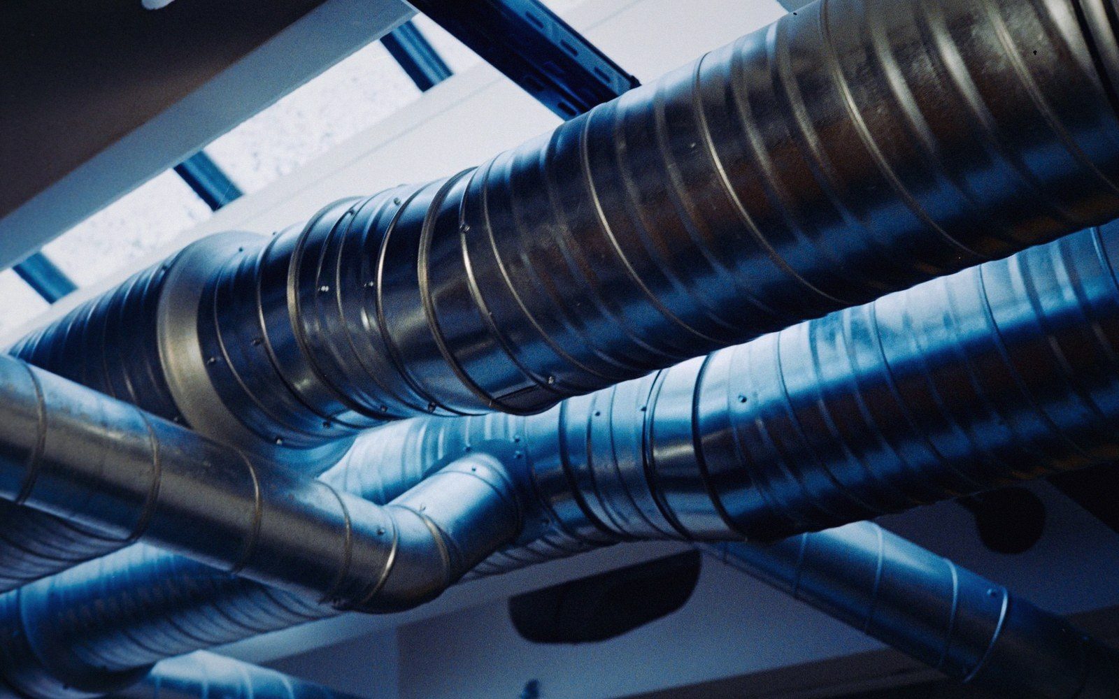 Metal spiral ductwork pipes run along a ceiling, branching in different directions
