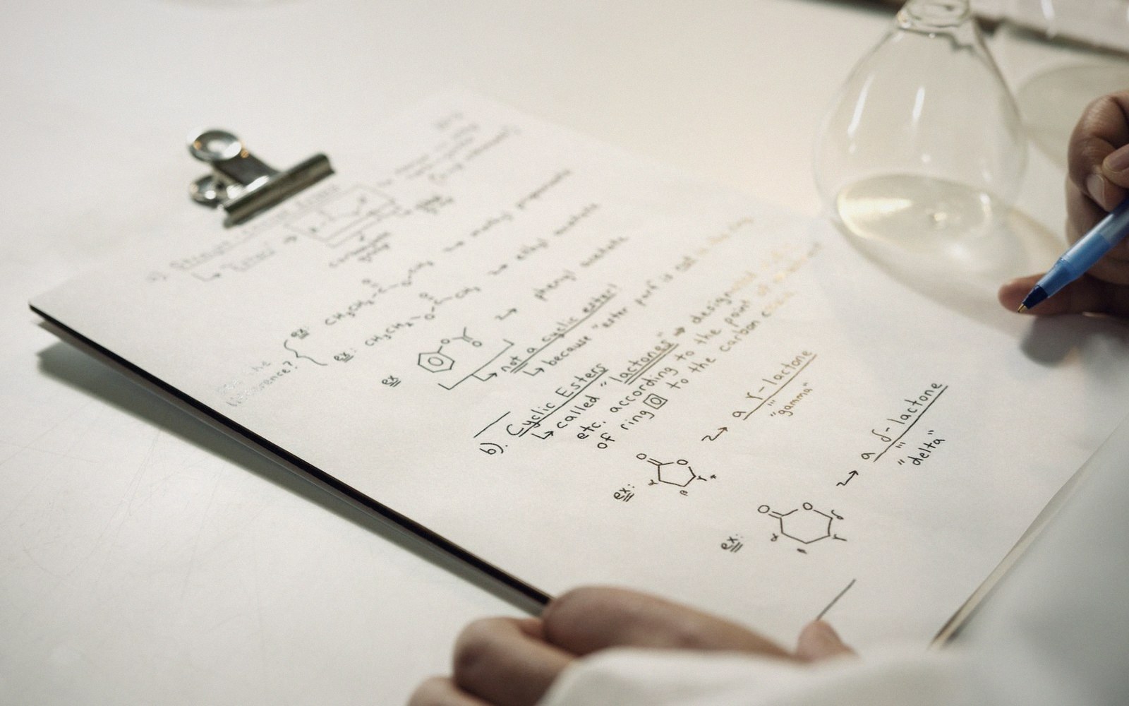 Handwritten notes on cyclic esters and lactones with molecular diagrams on a clipboard