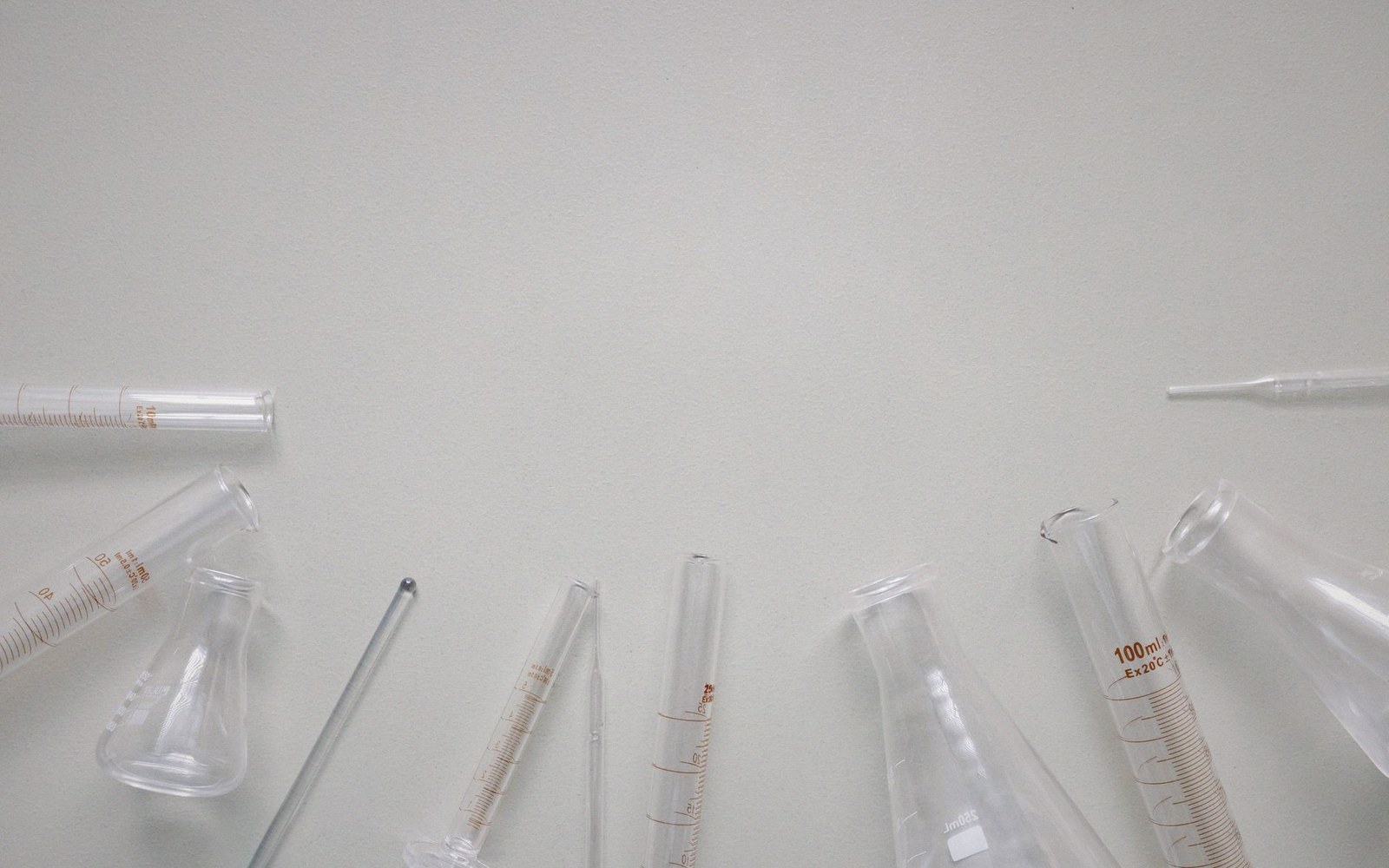 Empty glass laboratory flasks, test tubes and pipettes arranged along the bottom edge