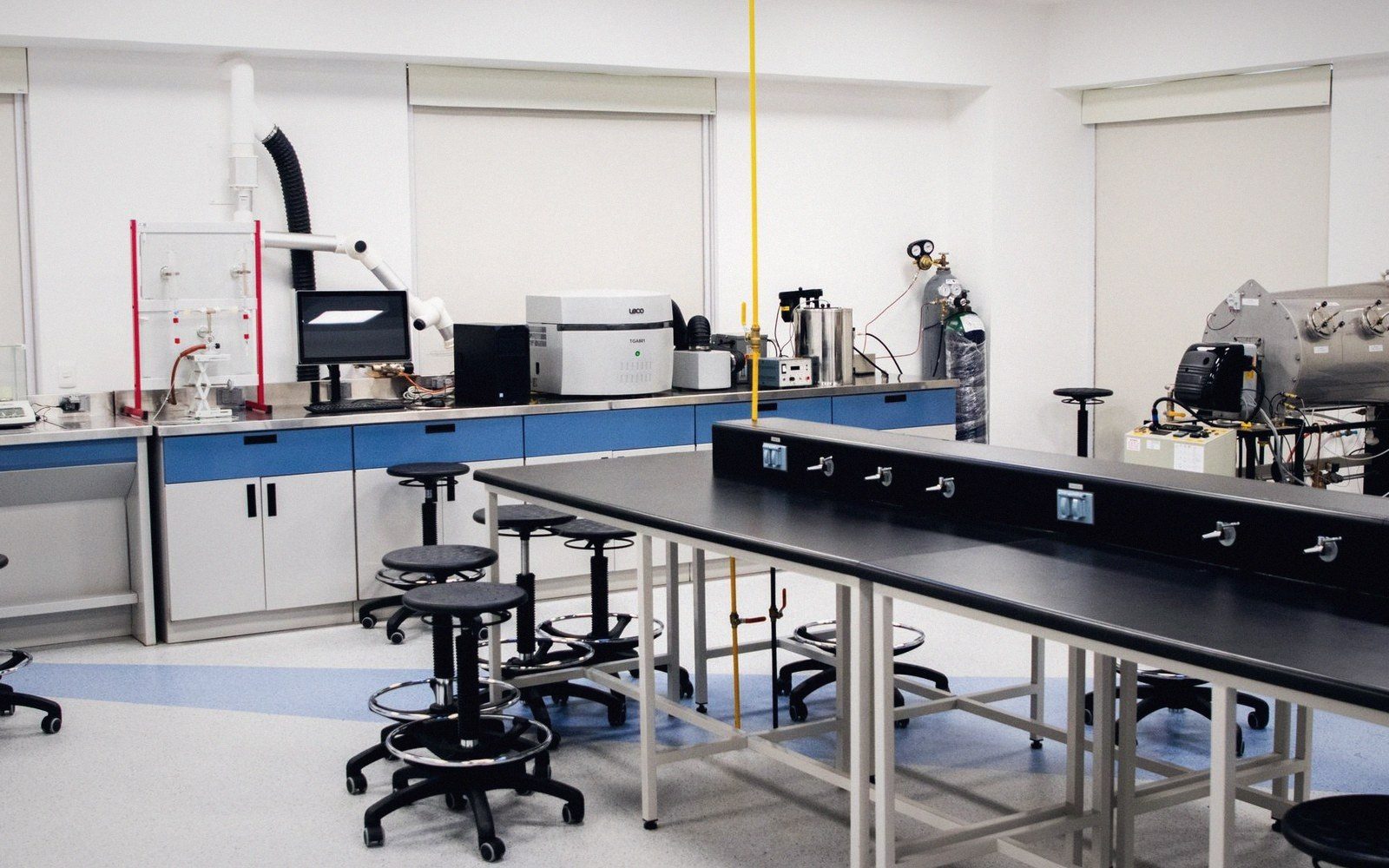 Empty laboratory with black lab benches, stools and analytical instruments along the wall