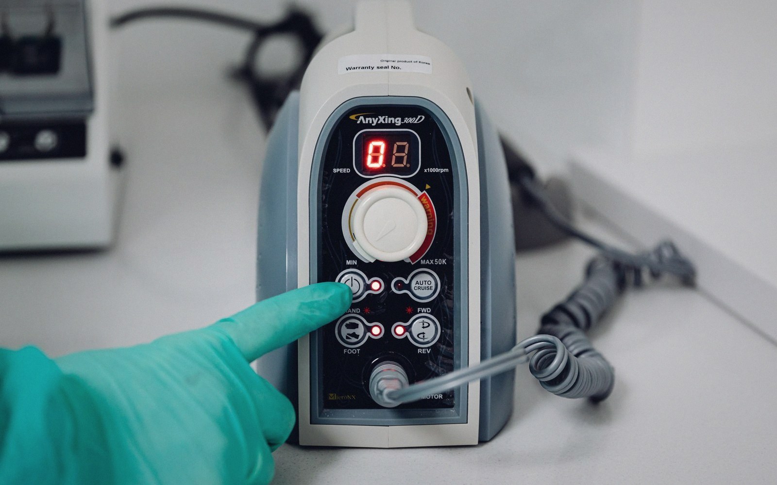A gloved finger presses a button on a dental micromotor control unit's display panel