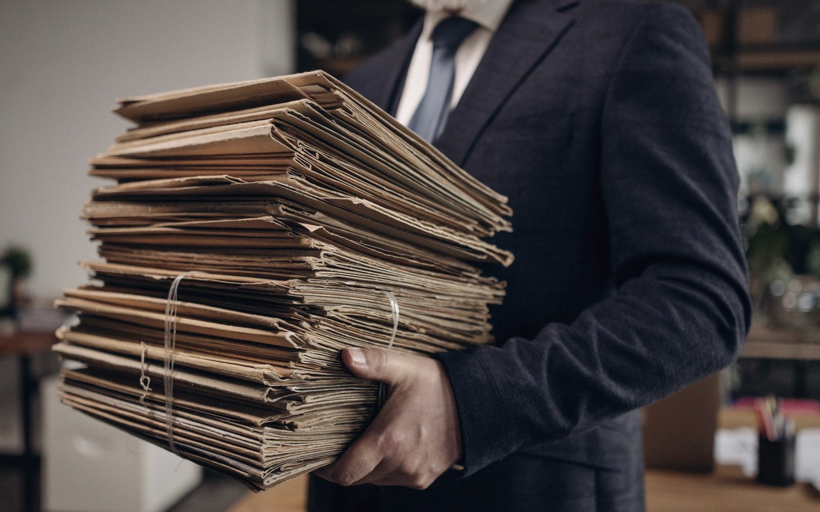 A man in a suit carries a large stack of worn cardboard folders