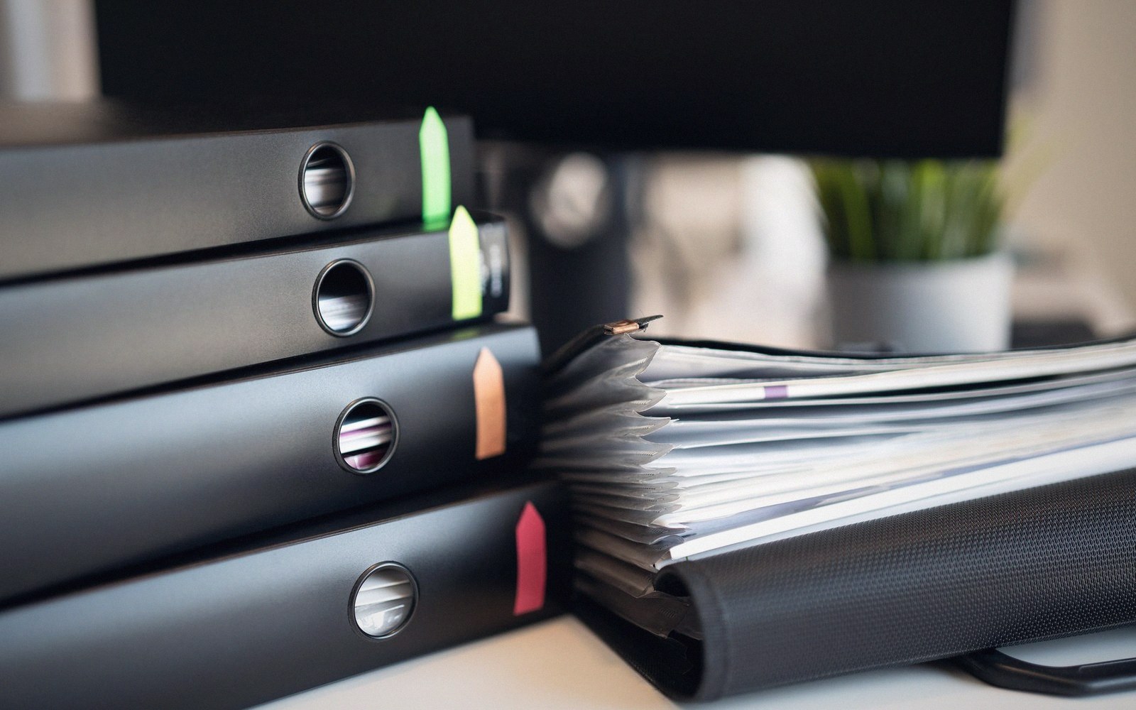 Stacked black binders with colored tab markers beside an open file thick with paper documents