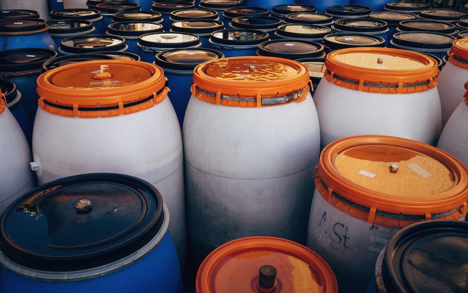 Rows of white and blue plastic storage barrels with orange and black lids